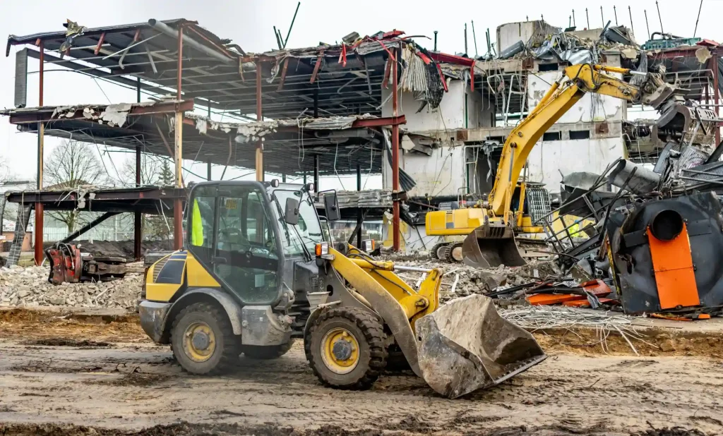 Construction site with heavy machinery, including a bulldozer and excavator, actively involved in the demolition of a multi-story building.