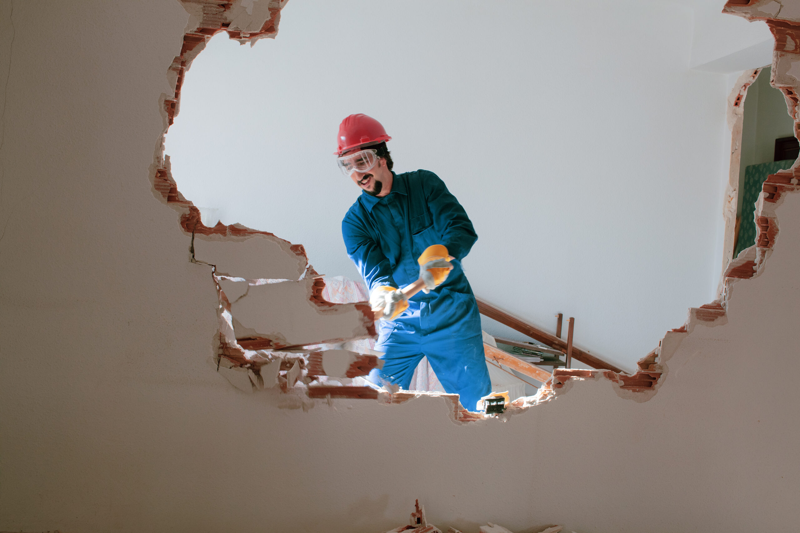 demolition contractors Young worker in red helmet and blue suit performing interior demolition