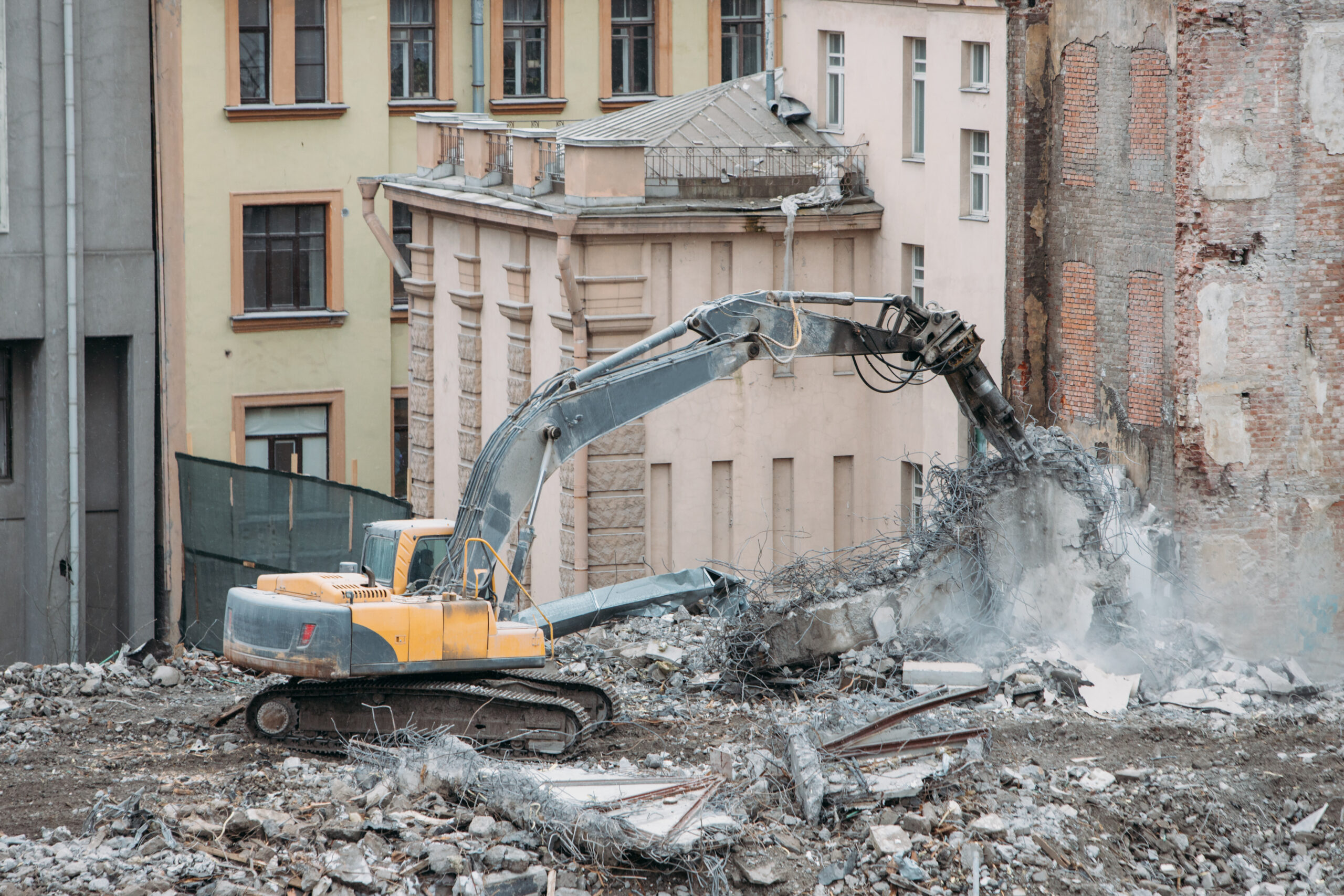 exterior-demo-section-01 Excavator tearing down a building wall during an exterior demolition project in an urban area.